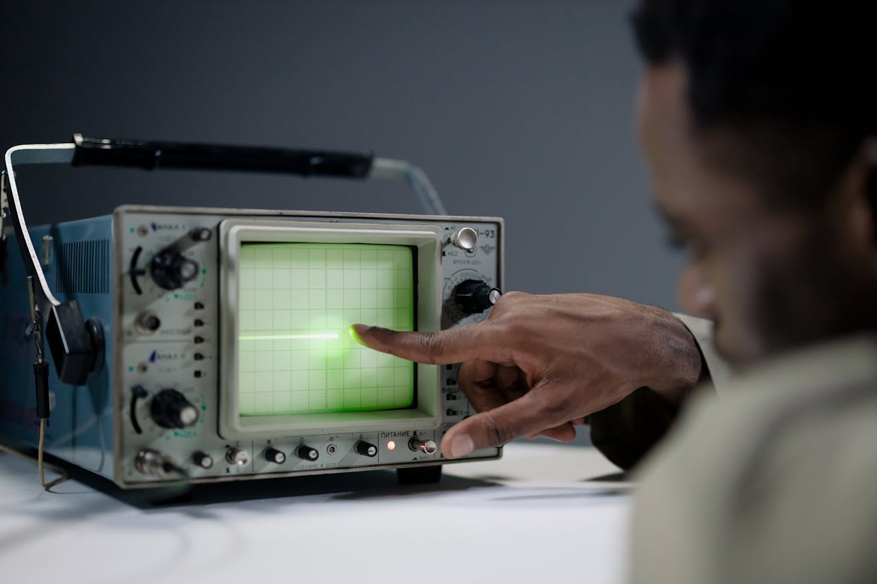 Close-up of a person pointing at a vintage oscilloscope screen in a tech setting.